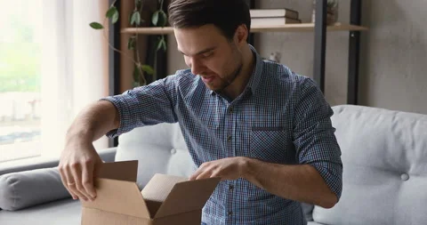 Guy opening delivered parcel feels satisfied by online purchase Stock Footage 134319865