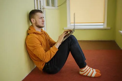 A guy in orange clothes sits on the floor with a laptop Stock Photos