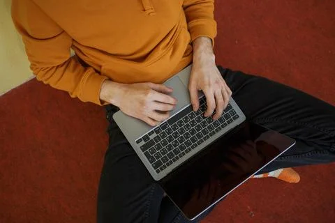 A guy in orange clothes sits on the floor working at a laptop Stock Photos