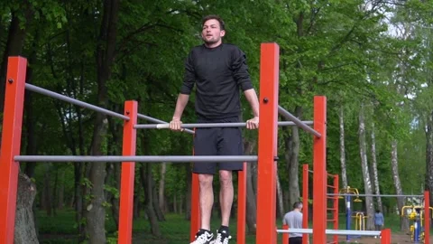 Guy is outdoors and pulling up on a horizontal bar. Steady shot, slow motion Stock Footage 130387415