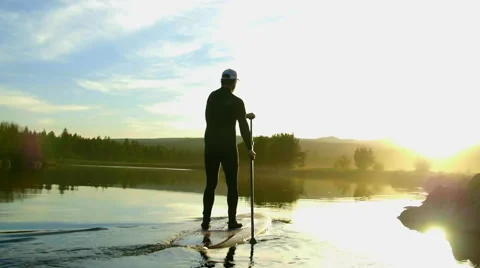 Guy paddle boards away into distance Stock Footage 63386103