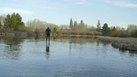 Guy paddle boards away down river Stock Footage 63386513