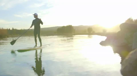 Guy paddle surfs on river past camera Stock Footage 64362682