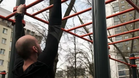 A guy passes a horizontal ladder on his hands, on a sports field on the street Stock Footage 238000321
