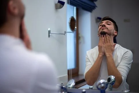 A guy with a patchy beard looks in the mirror Foto stock