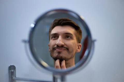 A guy with a patchy beard looks in the mirror Foto stock