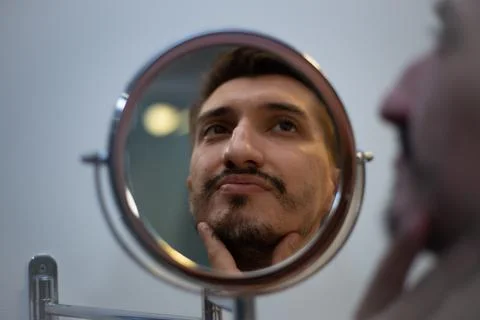 A guy with a patchy beard looks in the mirror Foto stock