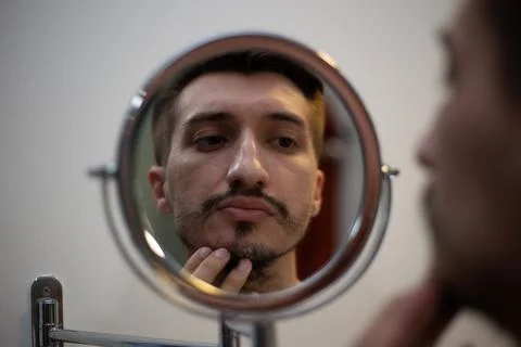 A guy with a patchy beard looks in the mirror Stock Photos