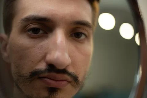 A guy with a patchy beard looks in the mirror Foto stock