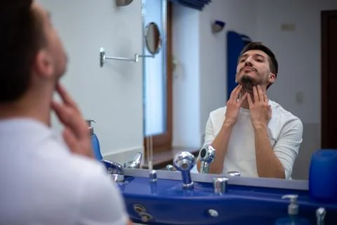 A guy with a patchy beard looks in the mirror Foto stock