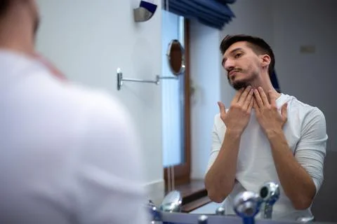 A guy with a patchy beard looks in the mirror Foto stock