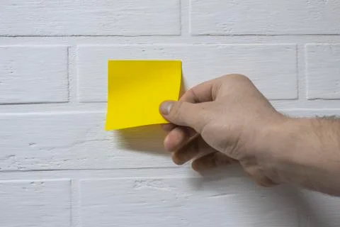 The guy peels off the yellow sticker for notes on the background of a white b Stock Photos