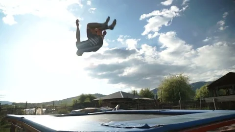 Guy performs acrobatic jumping on a trampoline against a background of mountains Stock Footage 77092045