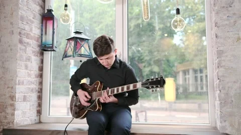 Guy performs jazz, blues music on guitar, sitting on windowsill in bar Stock Footage 135356469