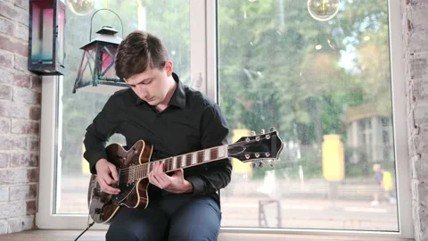 Guy performs jazz, blues music on guitar, sitting on windowsill in bar Stock Footage 135356485