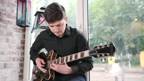 Guy performs jazz, blues music on guitar, sitting on windowsill in bar Stock Footage 135356532