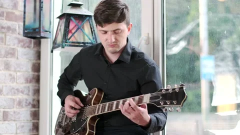 Guy performs jazz, blues music on guitar, sitting on windowsill in bar Stock Footage 135356975