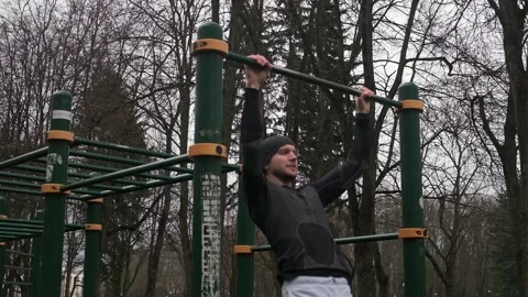 A guy performs a pull-up exercise on a horizontal bar on a sports field on the Stock Footage 237986634