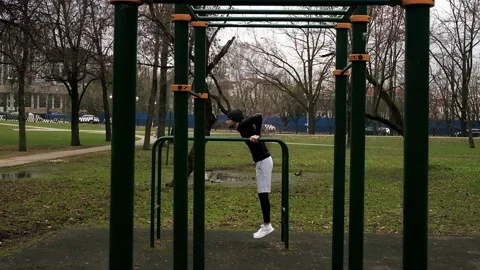 A guy performs a push-up exercise on the uneven bars on a sports field on the Stock Footage 237986939