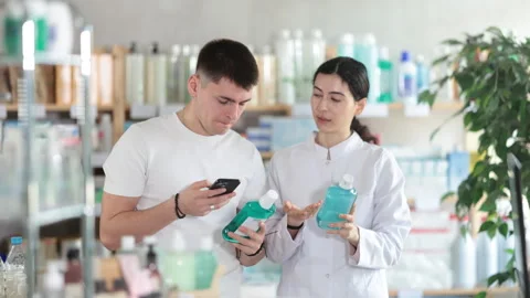 Guy in pharmacy scans QR code mouthwash product. Girl pharmacist offer help and Stock Footage 315030249