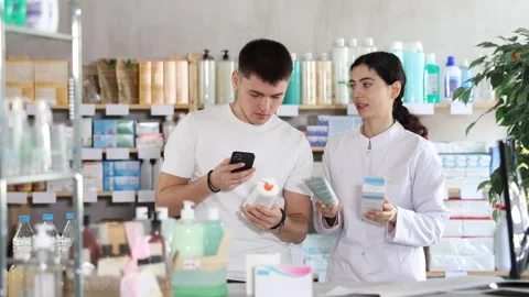 Guy in pharmacy scans QR code on emollient cream. Pharmacist offer help and Stock Footage 328138048