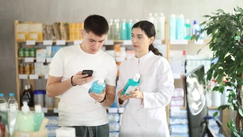 Guy in pharmacy scans QR code mouthwash product. Girl pharmacist offer help and Stock Footage 330042165