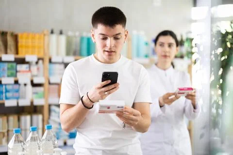 Guy in pharmacy scans QR code on tablet paracetamol, pharmacist i background Stockfoto's