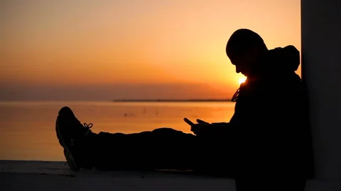 A guy with a phone in his hands Is sitting Admiring the sunset on the sea 库存影片 150281006