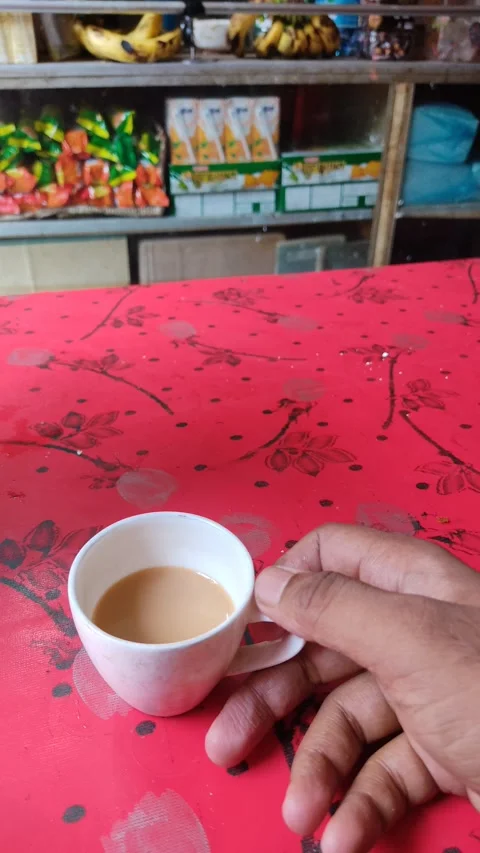 A guy piking up a small cup of milk tea from a red table in a tea stall Stock Footage 171417141