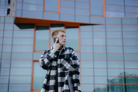 A guy in a plaid shirt talking on a mobile phone against the backdrop of a bu Stock-Fotos