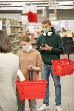 Guy with plastic shopping baskets using smartphone in queue by checkout counter Stock Photos