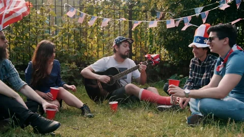 Guy playing guitar with friends sitting in circle on the grass for 4th of July Stock Footage 133620125