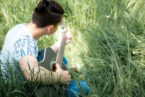 A guy playing a guitar sitting in the back Stock Photos