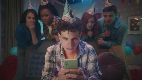 A guy is playing an online game on phone, his friends are watching him standing Stock Footage 242039668