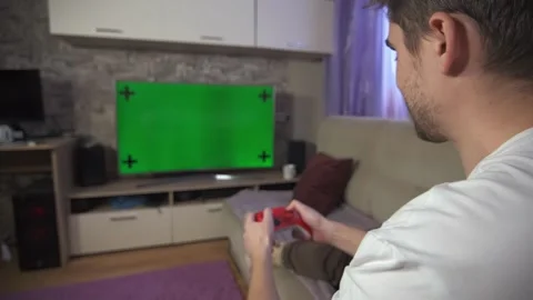 A guy plays a console in front of the TV, a green screen on the TV Stock Footage 264100114