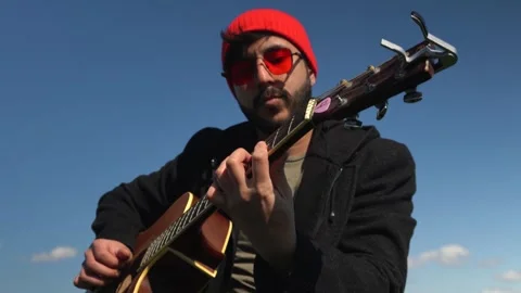 Guy plays the guitar. blue sky in the background. close-up. brunette in red hat Stock Footage 246294696