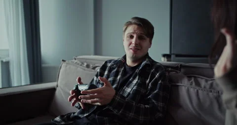 A guy plays video games using a joystick while his girlfriend asks for attention Stock Footage 305777568