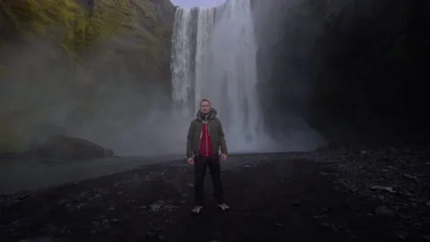 A guy poses in front of the backdrop of the huge Skogafoss waterfall 스톡 동영상 130474375