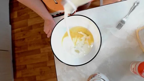 The guy pours milk into a plate of eggs. The view from the top Stock Footage 134424371