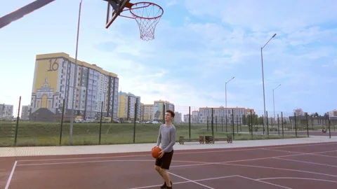 Guy practicing alone on a street basketball court to put the ball in the basket Stock Footage 204990701