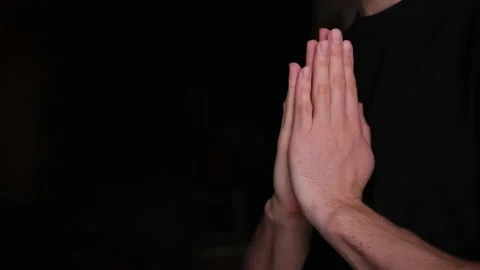 The guy prays. a man folded his hands in a prayer silhouette against a black blu Stock Footage 146835277