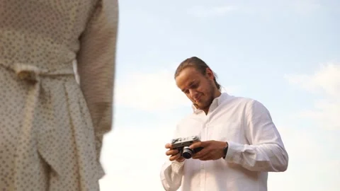 Guy prepares shoot with a girl on a silver film photo appart in field at sunset Stock Footage 160457680