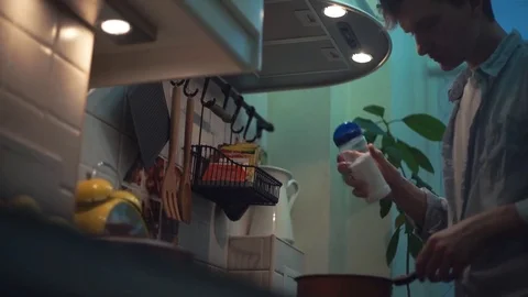 Guy preparing dinner in pot on stove in kitchen. stirs wooden spoon Stock Footage 83086786