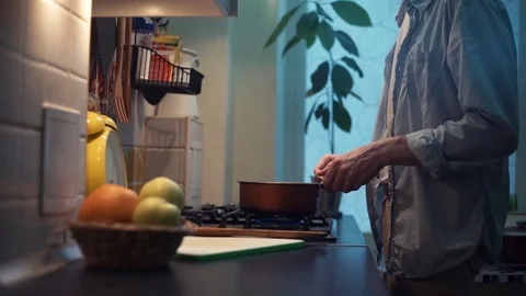 Guy preparing meal in pot on stove in kitchen. stirs wooden spoon Stock Footage 83039923