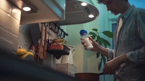 Guy preparing meal in pot on stove in kitchen, using tablet computer Stock Footage 83086977