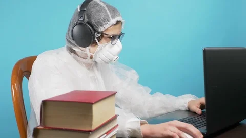 A guy in a protective mask and suit uses a laptop and books. blue background Vídeo Stock 126610677