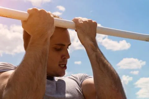 The guy pulls up on the bar. Workout outdoors. Blue sky on blackground Foto stock