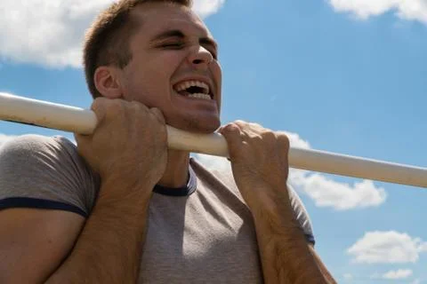 The guy pulls up on the bar. Workout outdoors. Blue sky on blackground Stock Photos