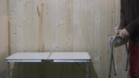 The guy put a folding stool in front of the table and sits on it Vidéo 119554382