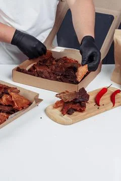 A guy puts dried meat in paper boxes in black gloves Stock Photos